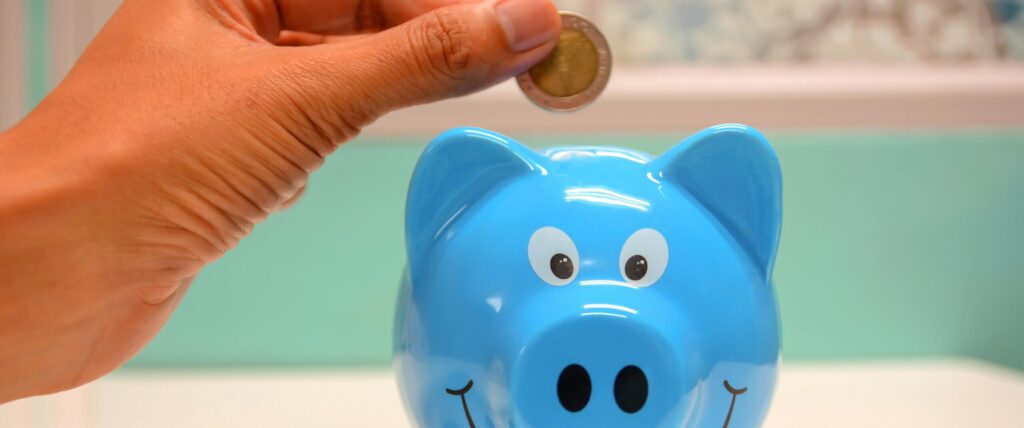 Hand inserting a coin into a blue piggy bank for savings and money management.